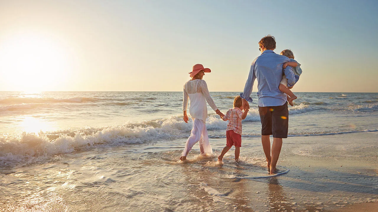 Eine Familie macht Urlaub und läuft Hand in Hand am Strand entlang durch die Wellen.